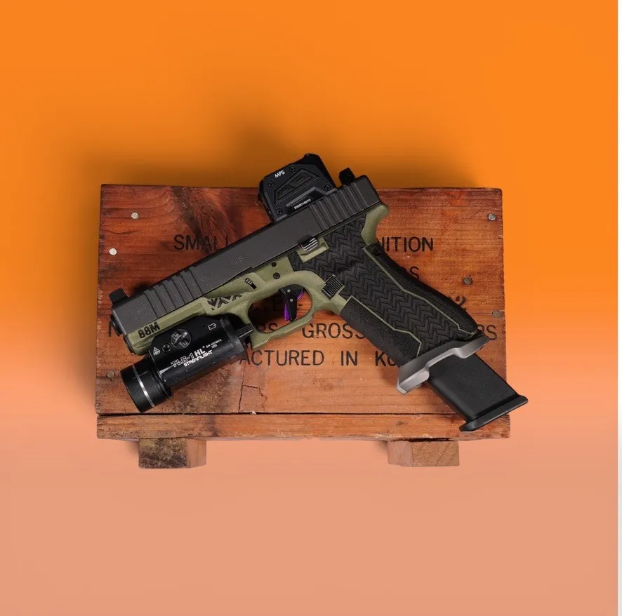 Glock pistol with an OD green Cerakote frame, black slide and stippled grip on an ammo crate