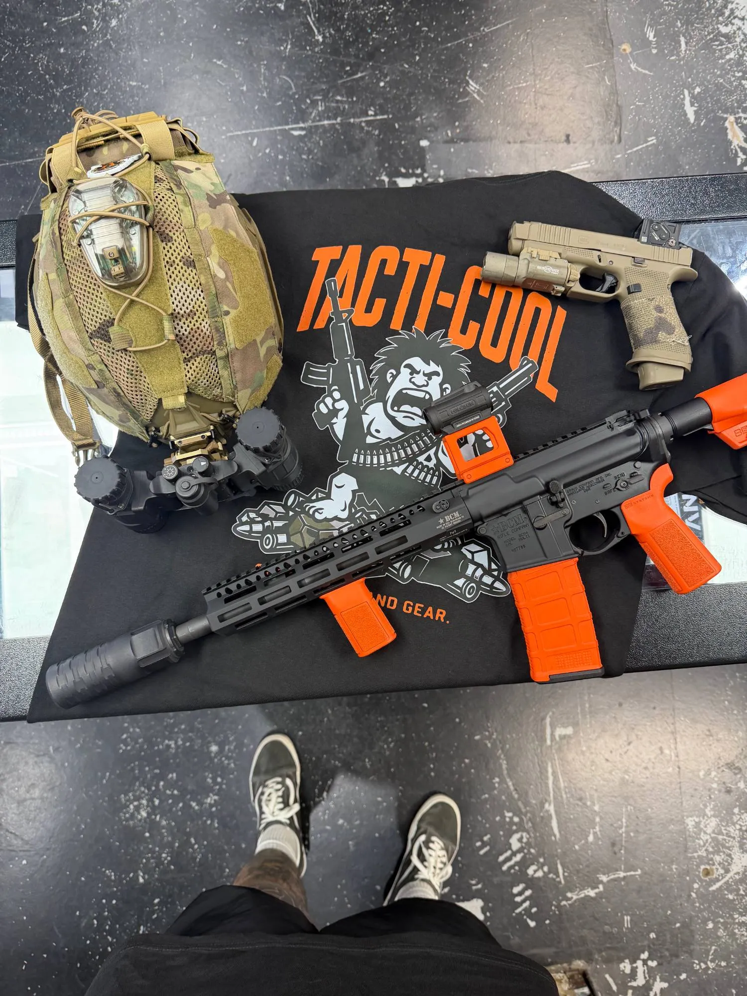 Black AR-style rifle with orange accents on a Tacti-Cool shirt next to an FDE pistol