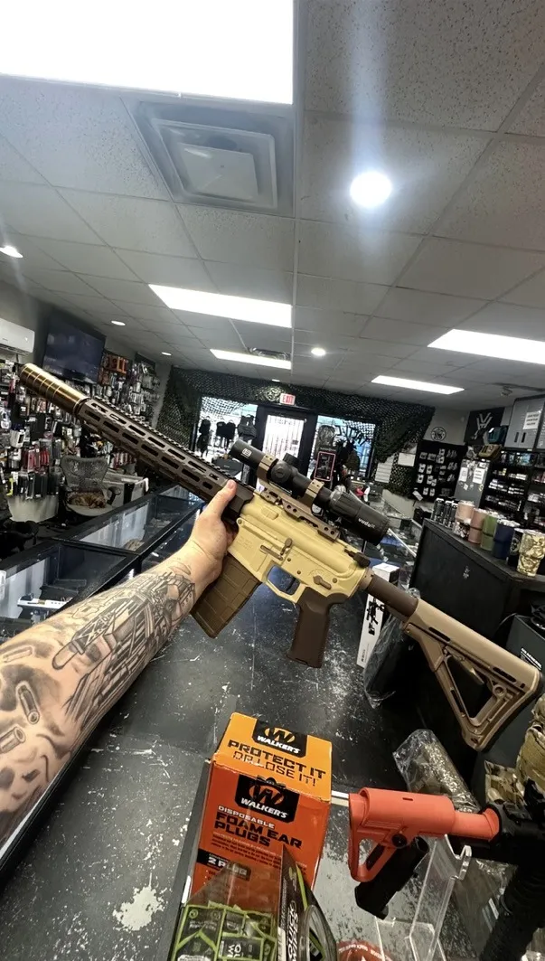 AR-style rifle with a tan receiver and bronze handguard, grip and stock, held up in the shop